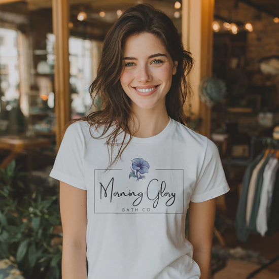 Smiling woman wearing a white Morning Glory Bath Co logo t-shirt in a sunlit indoor shop setting video