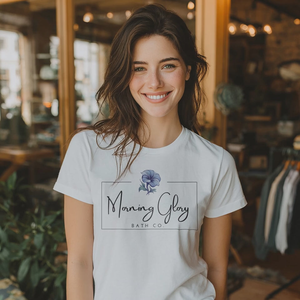 Smiling woman wearing a white Morning Glory Bath Co logo t-shirt in a sunlit indoor shop setting video